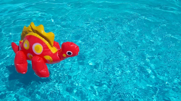 Inflatable dinosaur in clean rippling pool water. Summer vacation sale concept. A red children's toy floats isolated in blue water. Copy space for text