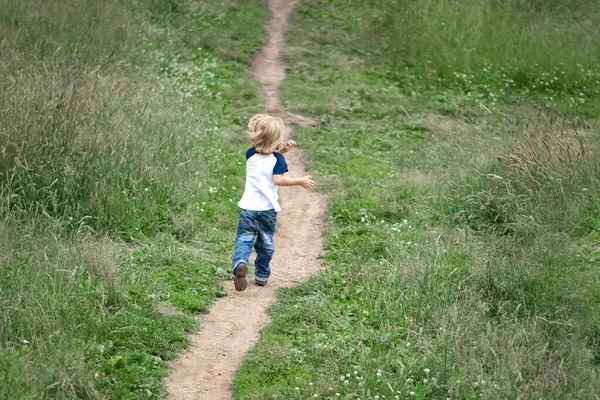 small boy runs away along the path at summer green meadow