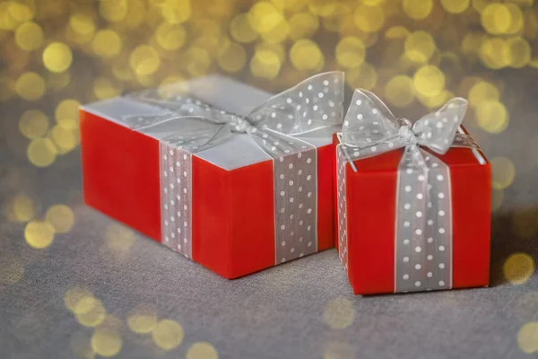 Two red gift boxes wrapped with white bow on neutral background with golden bokeh