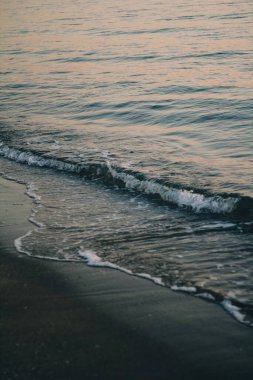 Dalganın tepesinde beyaz deniz köpüğü. Kaynayan su. Dalga kıyıya doğru ilerliyor. Şafakta deniz dalgaları.