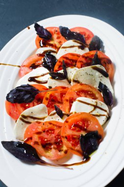 İtalyan Caprese salatası. Malzemeler mozzarella peyniri, domates, fesleğen, tuz, biber, balsamik. Yakın, koyu arka plan
