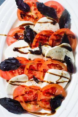 İtalyan Caprese salatası. Malzemeler mozzarella peyniri, domates, fesleğen, tuz, biber, balsamik. Yakın, koyu arka plan