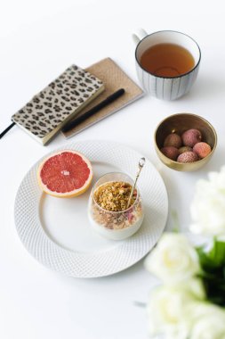 Sağlıklı bir kahvaltı iş. Malzemeler: greyfurt, granola, yoğurt, lychee, çay. Günlükleri tablo. Yan bakış, beyaz arka plan.