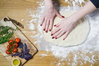 Şef Focaccia hazırlar. Çeşitler için malzemeler: hamur, domates, biberiye, kekik, fesleğen, zeytinyağı ahşap bir masa üzerinde. Üstten görünüm, ahşap arka plan