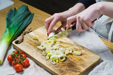 Şef, bir Ahşap Doğrama tahtası üzerinde pırasa keser. Arka plan mutfak, yan görünüm