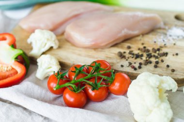 Ahşap Doğrama tahtası üzerinde çiğ tavuk göğsü. Malzemeler Bulgar biber, domates, pırasa, karnabahar, biber, tuz. Beyaz arka plan, yan görünüm