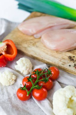 Ahşap Doğrama tahtası üzerinde çiğ tavuk göğsü. Malzemeler Bulgar biber, domates, pırasa, karnabahar, biber, tuz. Beyaz arka plan, yan görünüm