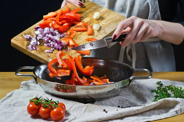 シェフは鍋にナイフで刻んだ赤ピーマンと玉ねぎを置きます 背景の台所 サイドビュー — ストック写真