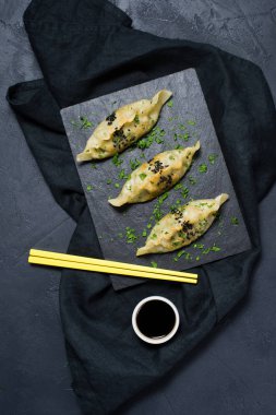 Kızarmış Kore köfte bir siyah üzerine kurulu taştan, yemek çubukları sarı. Koyu arka plan, üstten görünüm