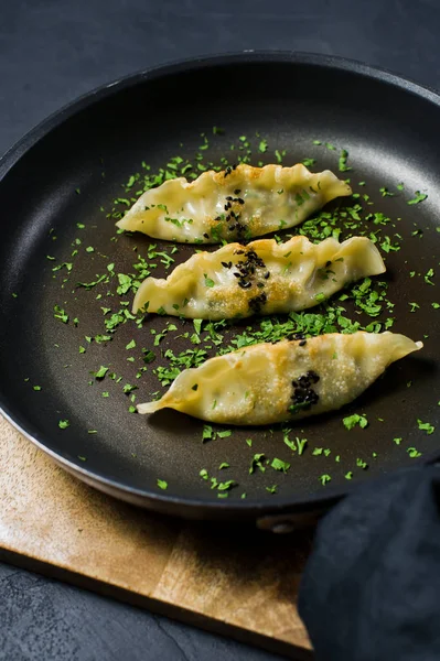 stock image Fried Japanese gyoza in a frying pan. Dark background, side view