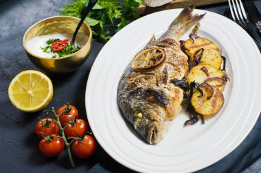 Dorado balık beyaz bir plaka üzerinde pişmiş, patates kızartması garnitür. Koyu arka plan, yan görünüm