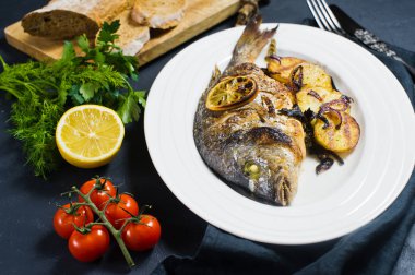 Dorado balık beyaz bir plaka üzerinde pişmiş, patates kızartması garnitür. Koyu arka plan, yan görünüm