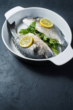 Çiğ Dorado balık Marine zeytin yağı, tuz ve biber, bir dilim limon üstte. Koyu arka plan, üstten görünüm, metin için yer