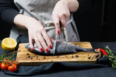 Eller Şef Dorado balık Ahşap Doğrama tahtası, madde biberiye, domates, biber, limon, kekik, biber, tuz kesti. Koyu arka plan, yan görünüm