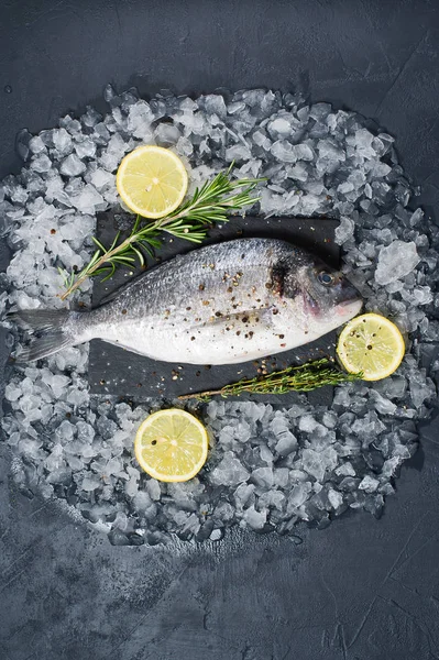 Dorado balık bir siyah Doğrama tahtası, madde biberiye, limon, ham buz. Koyu arka plan, üstten görünüm