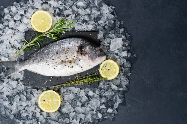 Dorado balık bir siyah Doğrama tahtası, madde biberiye, limon, ham buz. Koyu arka plan, üstten görünüm, metin için yer