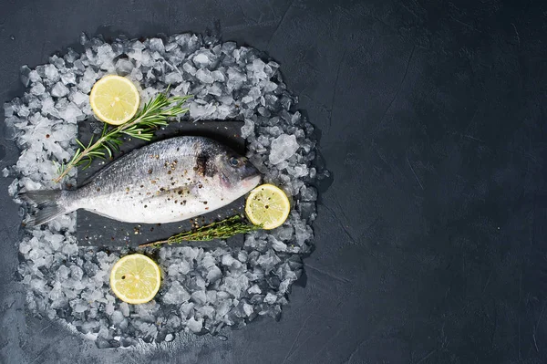 Dorado fish raw on a black chopping Board, ingredient rosemary, lemon, ice. Dark background, top view, space for text