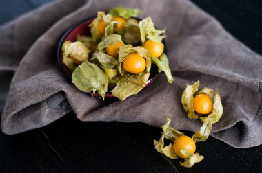 Çilek physalis siyah kase, koyu kumaş, koyu arka plan, üstten görünüm