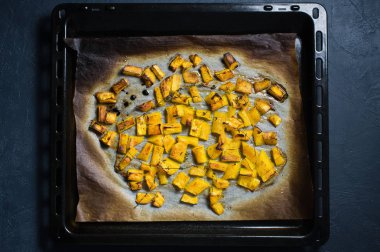 Bir fırın tepsisine fırın balkabağı. Koyu arka plan, üstten görünüm