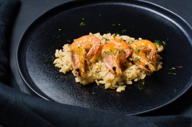 İtalyan risotto ile siyah bir tabak karides. Koyu arka plan, yan görünüm