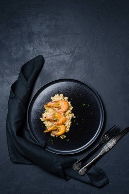 İtalyan risotto ile siyah bir tabak karides. Koyu arka plan, üstten görünüm, metin için yer