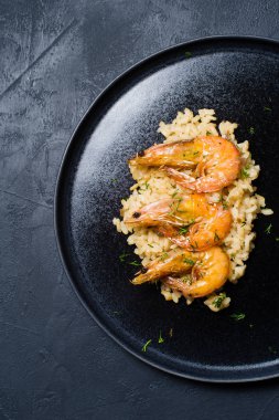 İtalyan risotto ile siyah bir tabak karides. Koyu arka plan, üstten görünüm, metin için yer