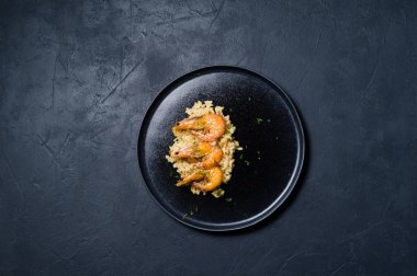İtalyan risotto ile siyah bir tabak karides. Koyu arka plan, üstten görünüm, metin için yer