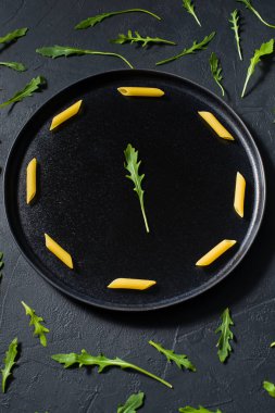 Roka ile Penne makarna kavramı minimalizm. Koyu arka plan, yan görünüm