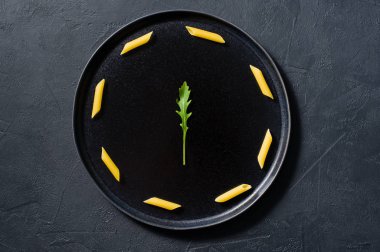 Roka ile Penne makarna kavramı minimalizm. Koyu arka plan, üstten görünüm