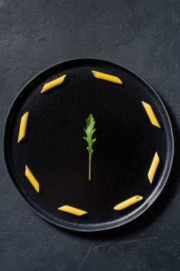 Roka ile Penne makarna kavramı minimalizm. Koyu arka plan, üstten görünüm