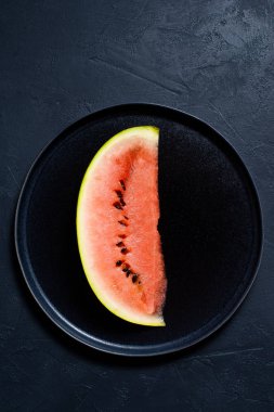 Bir dilim karpuz siyah bir plaka üzerinde. Koyu arka plan, üstten görünüm