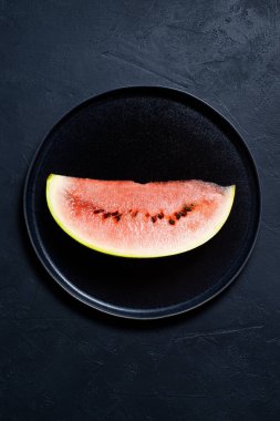 Bir dilim karpuz siyah bir plaka üzerinde. Koyu arka plan, üstten görünüm