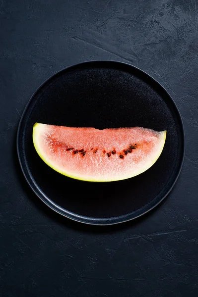 Bir dilim karpuz siyah bir plaka üzerinde. Koyu arka plan, üstten görünüm