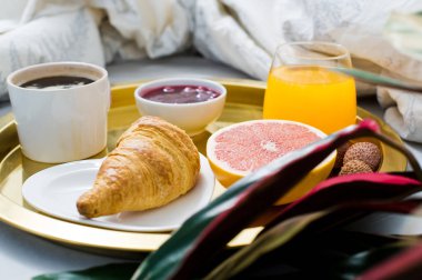 Yatakta, klasik Fransız kahvaltı ev dekorasyonu. Kahve, reçel, kruvasan, portakal suyu, greyfurt, lychee. Yan görünüm, açık renkli, kapat