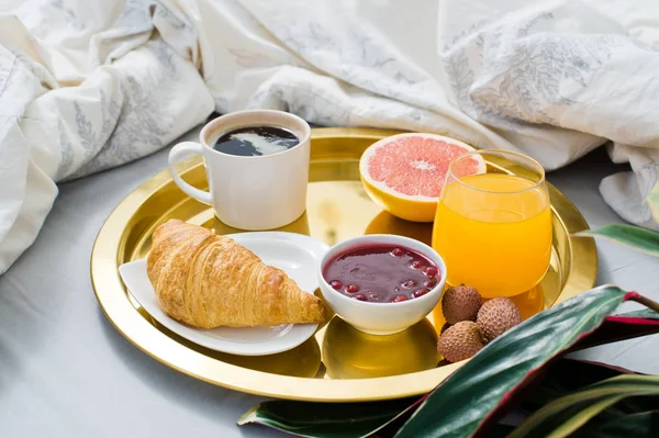 Breakfast in bed, hotel service. Coffee, jam, croissant, orange juice, grapefruit, lychee. Side view, light background