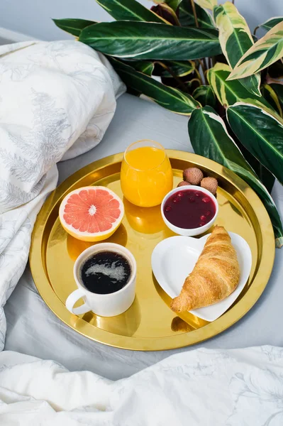Classic Breakfast in bed, hotel service. Coffee, jam, croissant, orange juice, grapefruit, lychee. Side view, light background