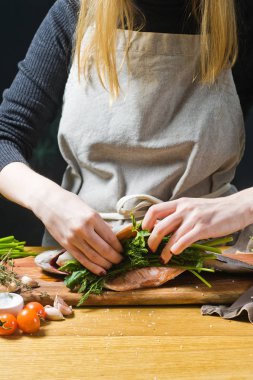 Şef ham alabalık maydanoz ve dereotu ile doldurulmuş. Malzemeler biberiye, limon, domates, sarımsak, tuz, karabiber. Siyah arka plan, yan görünüm