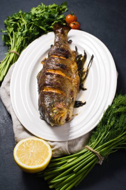 Beyaz bir levha, dal dereotu ve maydanoz üzerinde Izgara Alabalık. Siyah arka plan, yan görünüm