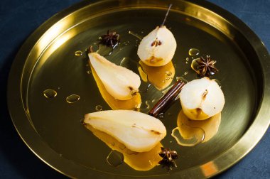 Altın tepside beyaz şarap pişmiş haşlanmış armut dilimlenmiş. Siyah arka plan, üstten görünüm