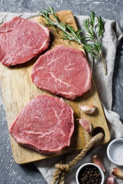 Üç sığır eti biftek Ahşap doğrama tahtası, sarımsak ve biberiye bir delikanlı. Üstten Görünüm, gri arka plan