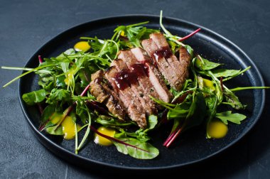 Dana bonfile, roka ve siyah bir tabak pazı salatası. Yan görünümü, siyah arka plan