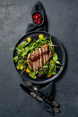 Sığır bonfile biftek, roka ve siyah bir tabak pazı salatası. Kızılcık sosu. Üstten Görünüm, siyah arka plan, metin için yer