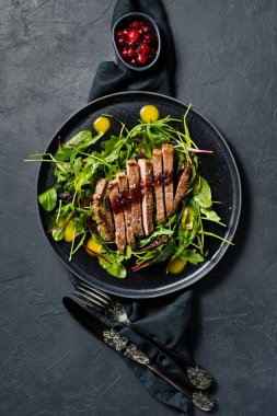 Sığır eti biftek, roka ve siyah bir tabak pazı salatası. Kızılcık sosu. Üstten Görünüm, siyah arka plan