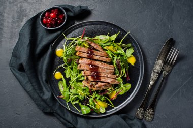 Sığır eti biftek, roka ve siyah bir tabak pazı salatası. Kızılcık sosu. Üstten Görünüm, siyah arka plan