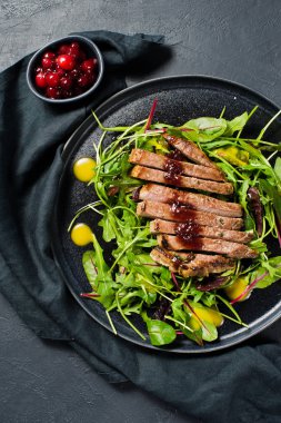 Sığır bonfile biftek, roka ve siyah bir tabak pazı salatası. Kızılcık sosu. Üstten Görünüm, siyah arka plan, metin için yer