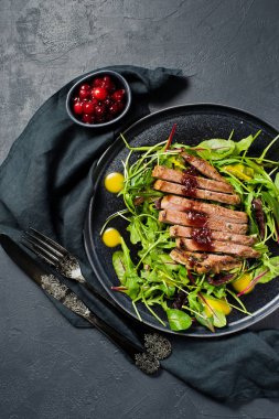 Sığır eti biftek, roka ve siyah bir tabak pazı salatası. Kızılcık sosu. Üstten Görünüm, siyah arka plan