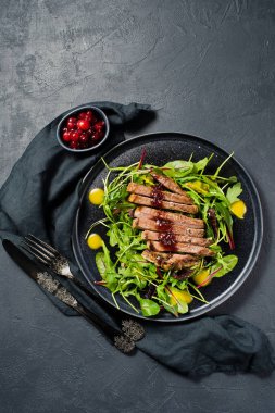 Sığır eti biftek, roka ve siyah bir tabak pazı salatası. Kızılcık sosu. Üstten Görünüm, siyah arka plan, metin için yer