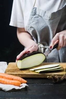 Elinde Şef ahşap kesme tahtası üzerinde patlıcan dilim. Yan görünüm, siyah arka plan, kapat