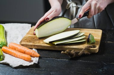 Elinde Şef ahşap kesme tahtası üzerinde patlıcan dilim. Yan görünüm, siyah arka plan, kapat