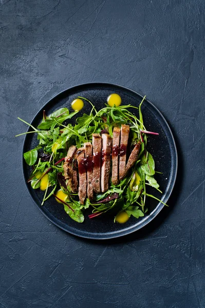 Salad with beef tenderloin, arugula and chard on a black plate. Side view, black background, space for text